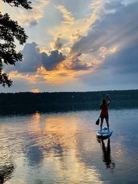 Man standing in lake against sky during sunset