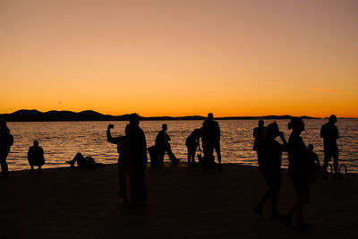 Silhouette people at beach against clear sky during sunset