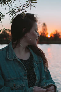 Beautiful woman standing by lake against sky during sunset