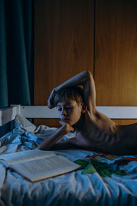 Shirtless boy reading book while lying on bed at home