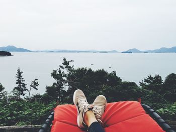 Low section of woman resting by lake against sky