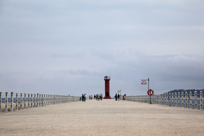 Bridge leading towards lighthouse against sky