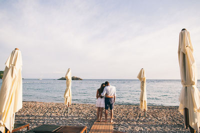 Rear view of people standing on beach against sky