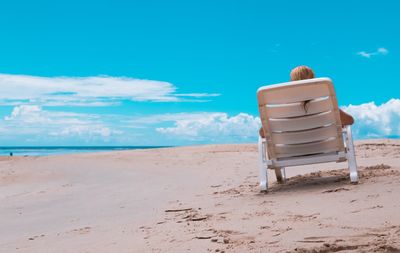 Person sitting on chair at beach against blue sky