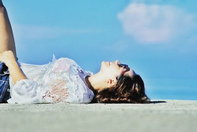 Side view of woman lying on road against blue sky