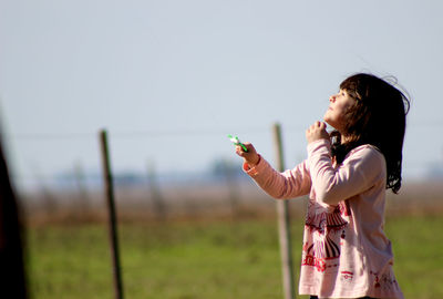 Side view of cute girl holding toy while standing on field