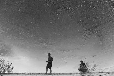 Men reflecting in puddle on footpath