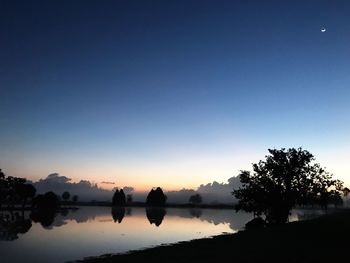 Silhouette trees by lake against sky during sunset