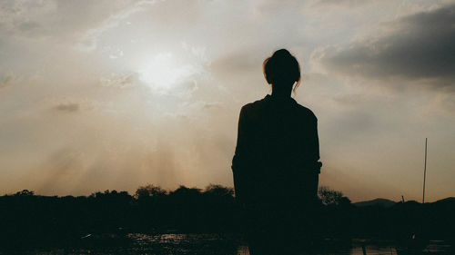 Silhouette girl standing on field against sky during sunset