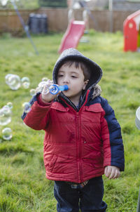 Boy blowing bubbles while standing at back yard