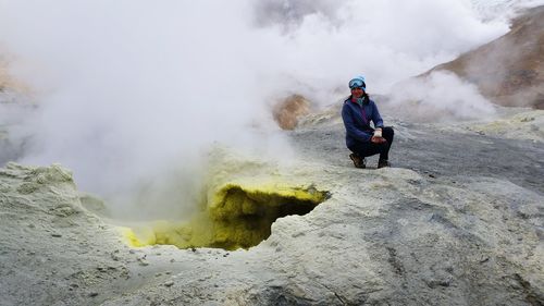 Woman crouching on rock against volcanic landscape