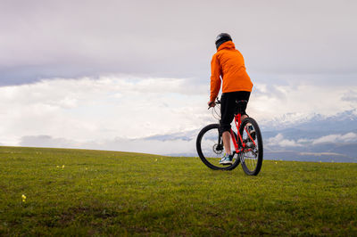 Rear view of man riding bicycle on field