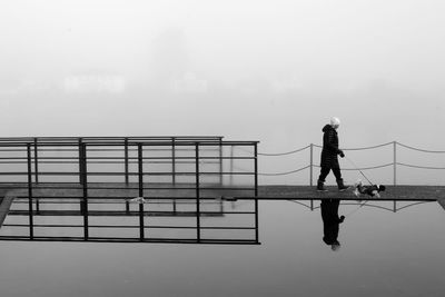 Person walking with dog on pier amidst lake against sky