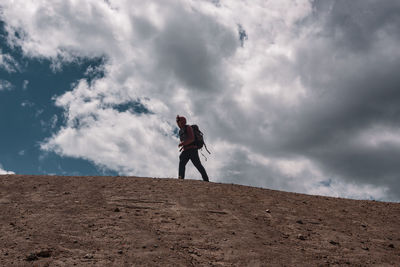 Low angle view of young man walking on mountain against cloudy sky