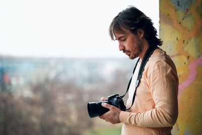 Side view of man holding camera against sky