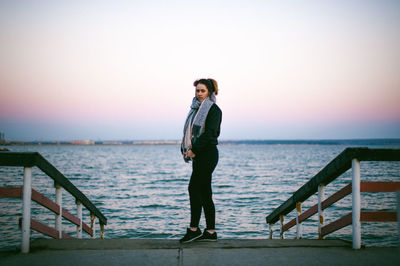 Full length portrait of young woman standing on beach against clear sky
