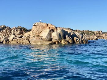 Rock formations in sea against clear blue sky