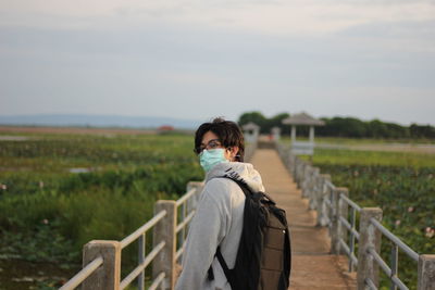 Side view of woman standing on railing against sky