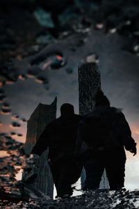 Two people standing by built structure against sky reflected in puddle 