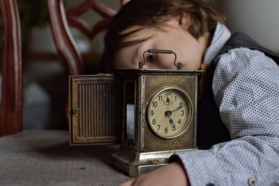 Close-up of boy with vintage clock on table