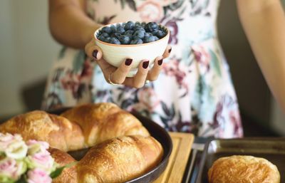 Midsection of woman holding bowl with blueberry fruits over bread
