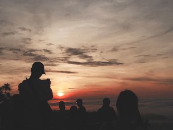 Silhouette people photographing sea against sky during sunset