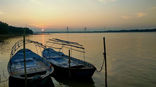 Boats moored in river against sky during sunset