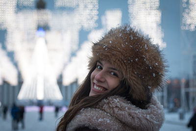 Portrait of smiling young woman standing against tree lights