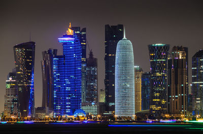 Illuminated tornado tower with burj qatar against sky at night