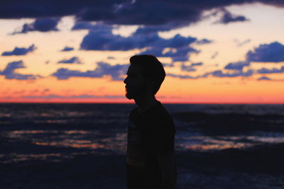 Silhouette man standing at beach against sky during sunset