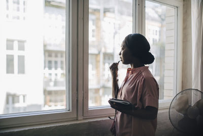 Young businesswoman talking through earphones while standing by window in creative office