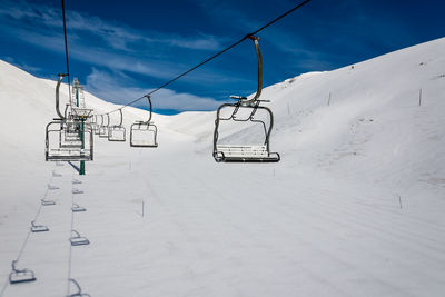 Ski lifts over snow covered landscape against sky