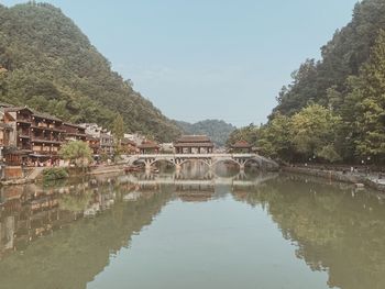 Arch bridge over lake by buildings against sky