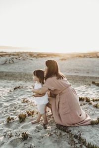 Side virew of mother embracing toddler twins at beach