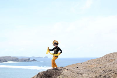 Man standing on rock by sea against sky