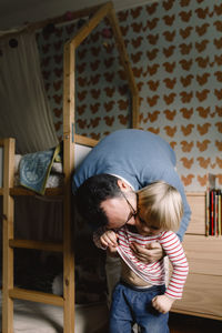 Father kissing daughter while dressing her in bedroom at home