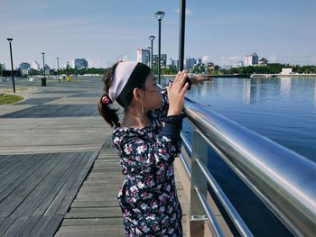 Young woman standing by railing against sky