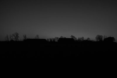 Silhouette trees on field against clear sky