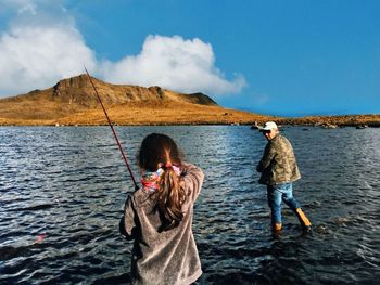 Rear view of friends and woman in sea against sky