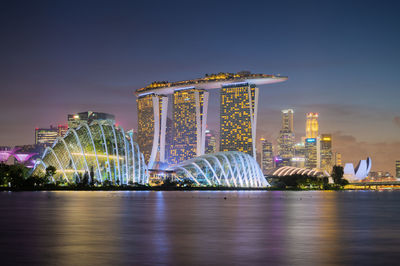 Illuminated city by sea against sky at night