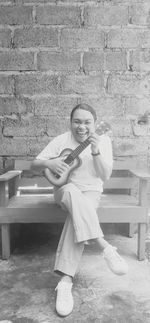 Portrait of smiling man sitting on bench against wall