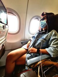 Woman wearing mask listening music while sitting at airplane