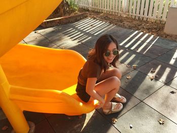 High angle view of smiling young woman wearing sunglasses sitting on slide in park