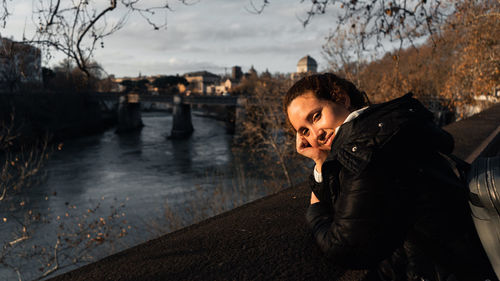 Portrait of young woman standing against river