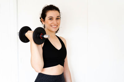 Portrait of young woman lifting dumbbells against white background