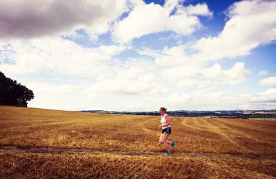 Side view of woman jogging on field against cloudy sky