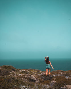 Rear view of woman standing on mountain by sea against sky