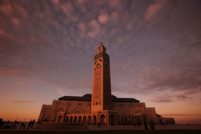 Low angle view of mosque hassan ii against cloudy sky during sunset in city