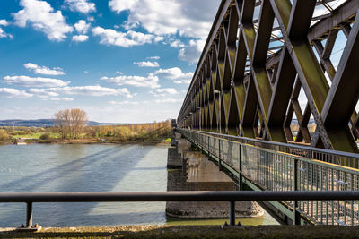 Steel, lattice structure of a railway bridge over a river with a background of blue sky with clouds