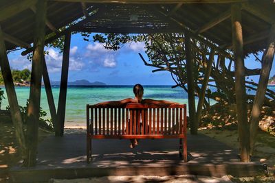 Rear view of woman relaxing on bench at beach